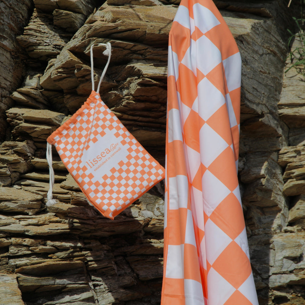 Orange and white checkered beach towel with matching drawstring bag, perfect for ocean adventures.