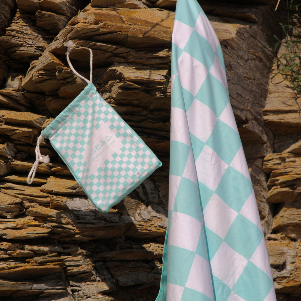 Mint and white checkered beach towel with matching drawstring bag, draped on coastal rocks