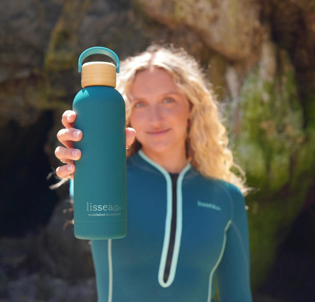Woman in teal springsuit holding matching Lissea water bottle with bamboo lid, ideal for beach adventures.