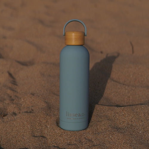 Lissea beach water bottle with bamboo lid on sand, perfect for ocean adventures and coastal style.