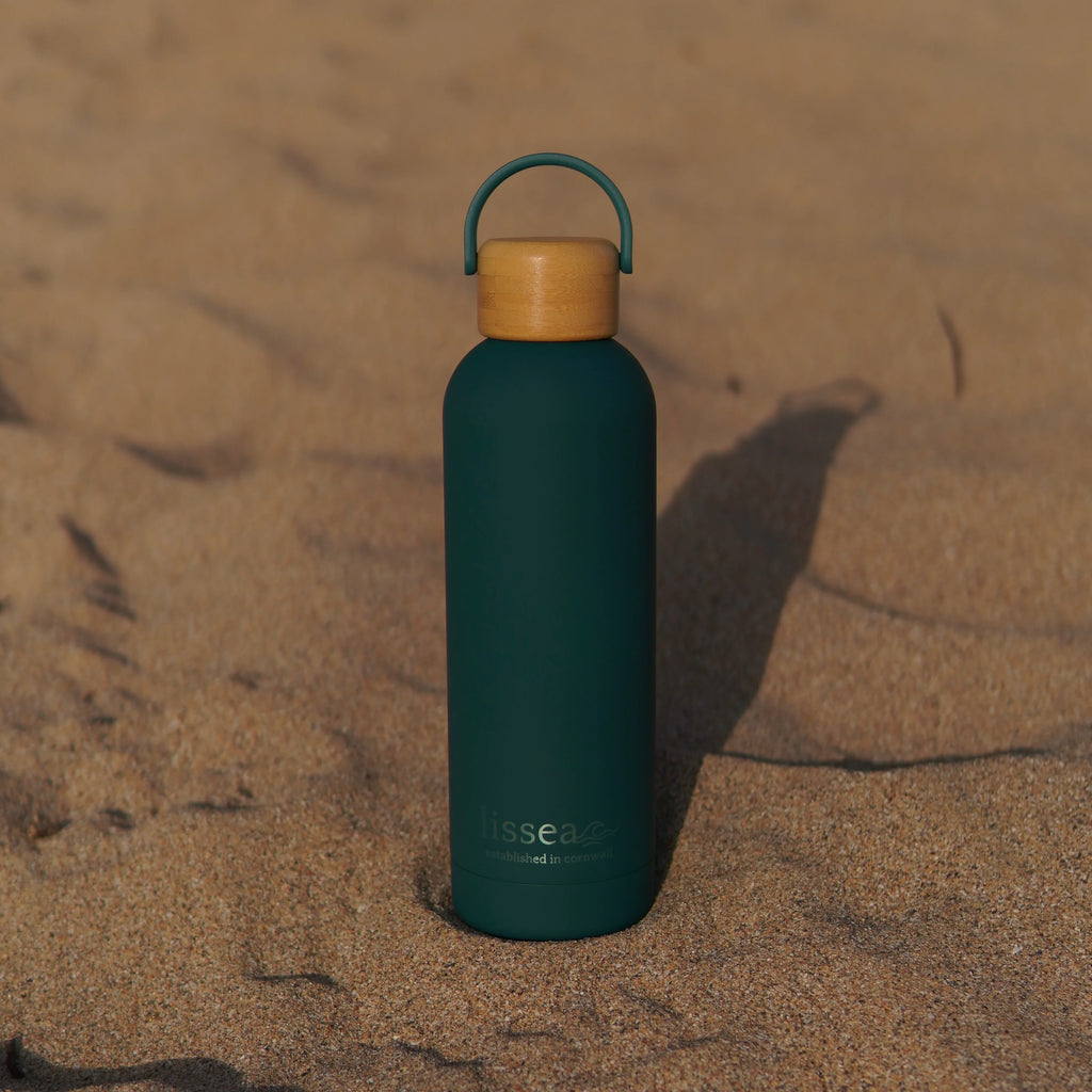 Teal beach water bottle with bamboo lid on sand, perfect for ocean adventures and sustainable hydration.