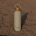 Lissea beach water bottle with bamboo lid on sandy shore, perfect for ocean adventures and coastal travel.