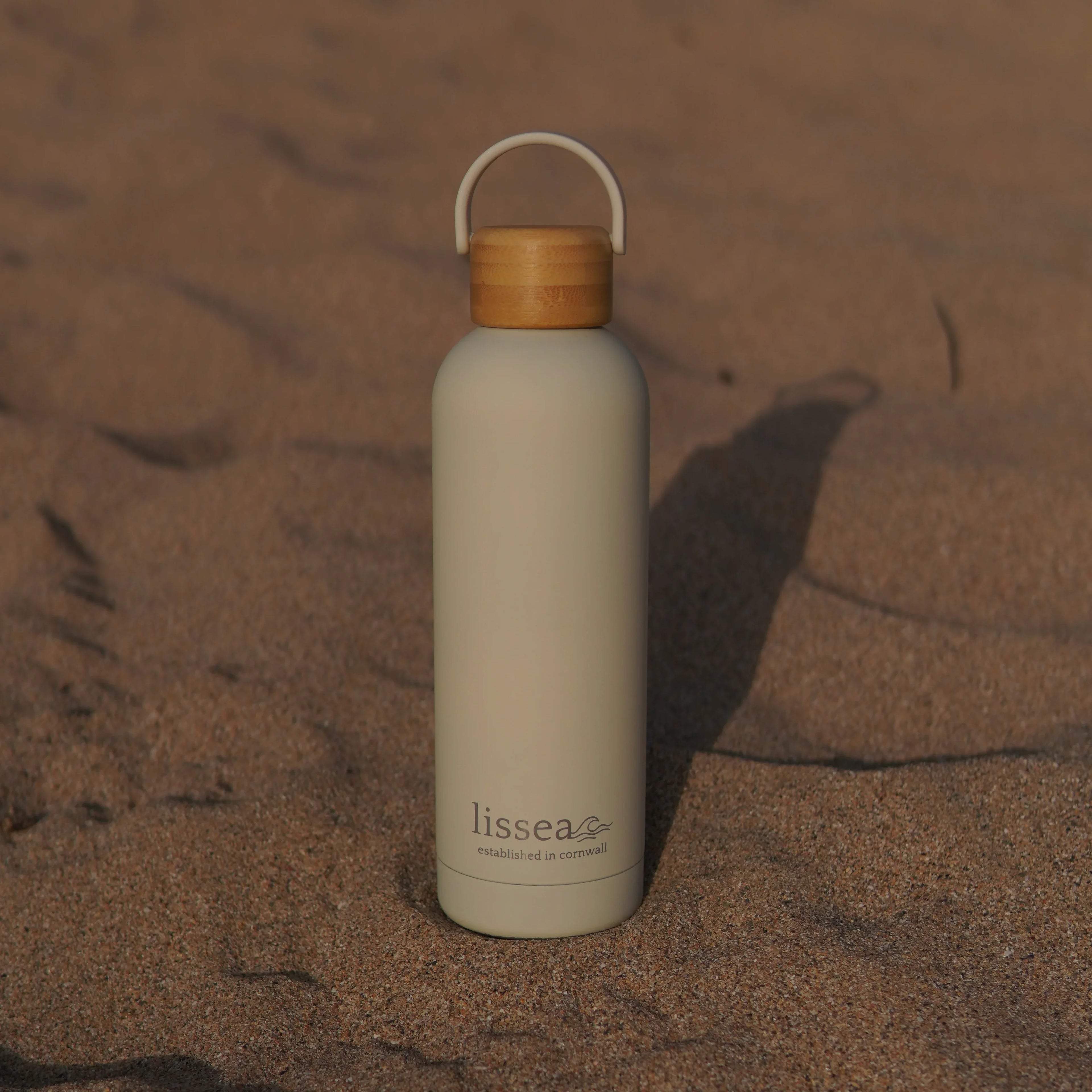 Lissea beach water bottle with bamboo lid on sandy shore, perfect for ocean adventures and coastal travel.