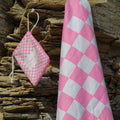 Pink and white checkered beach towel with matching drawstring bag against rocky coast