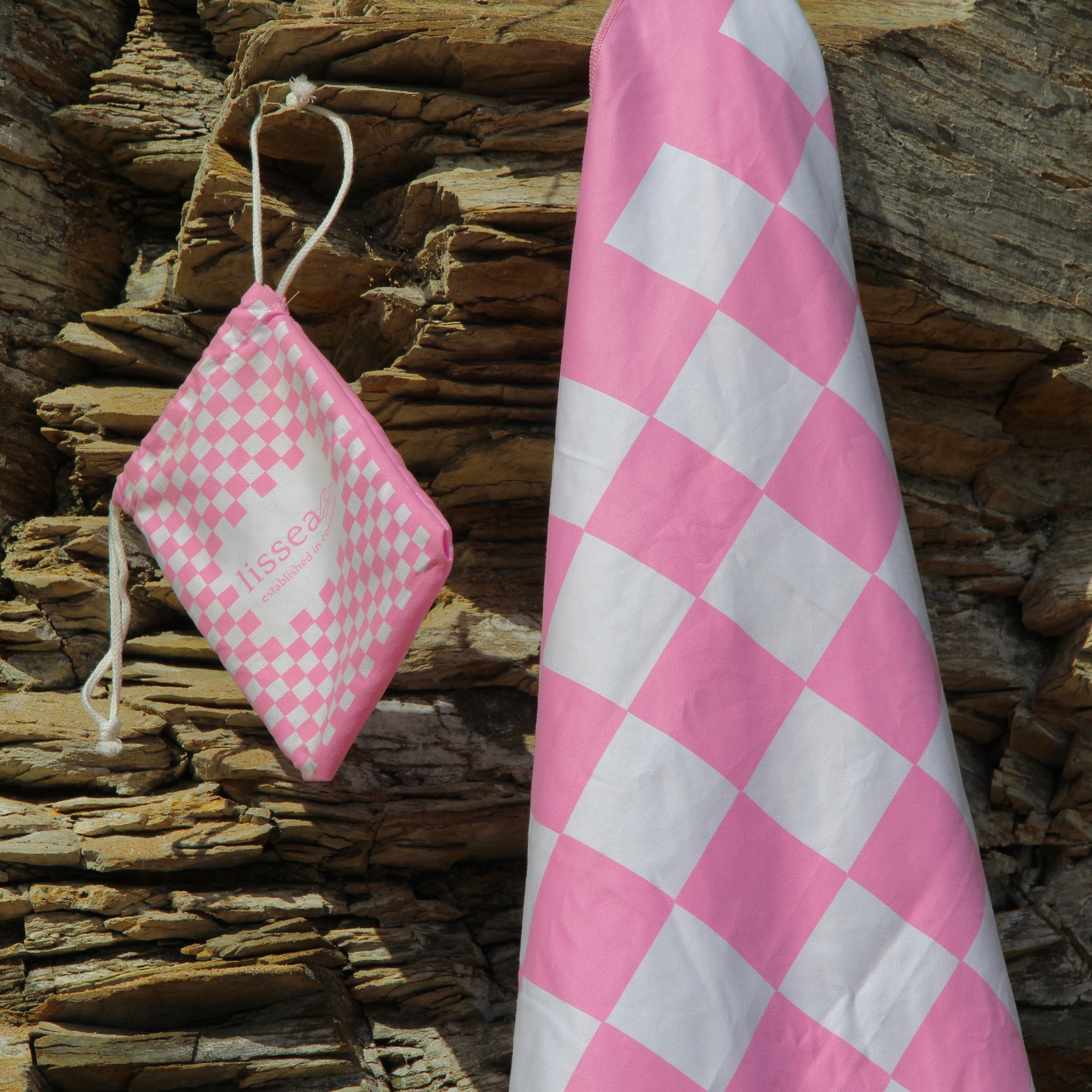 Pink and white checkered beach towel with matching drawstring bag against rocky coast