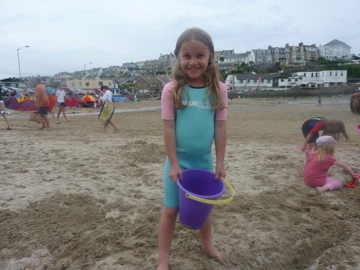 Girl in colorful springsuit holding purple bucket on sandy beach, perfect for ocean adventures