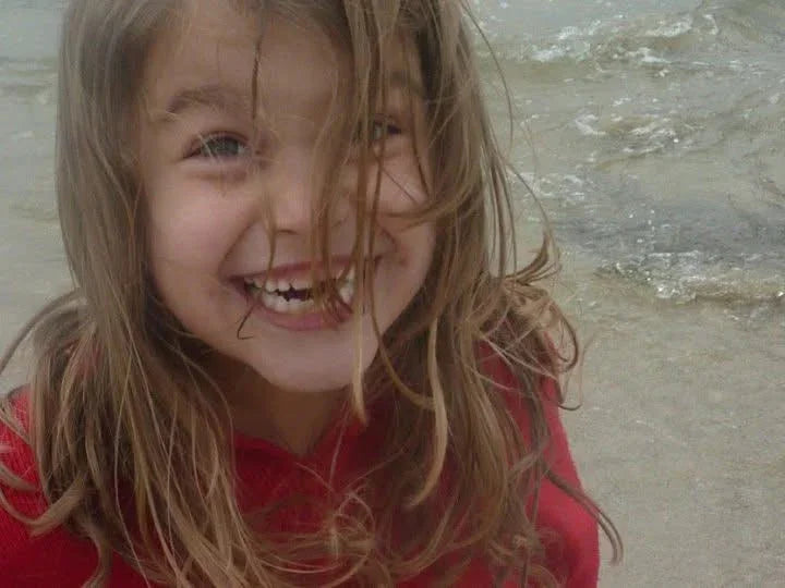 Happy girl in red springsuit smiling at beach, ocean waves behind