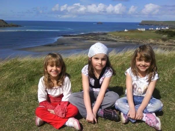 Three girls sitting on grassy cliff overlooking ocean, enjoying coastal scenery