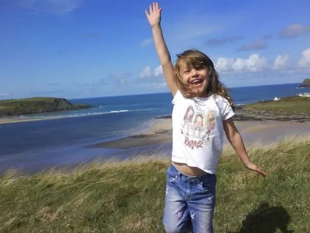 Happy girl waving on grassy coastal cliff overlooking ocean beach