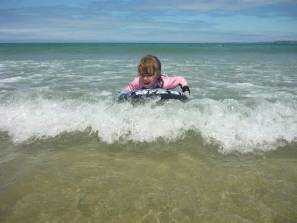 Child in pink springsuit riding wave on surfboard at beach